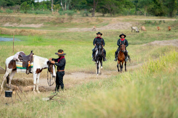 Fototapeta premium Two cowboys on horses are riding to the village after finish take care of cow in background.