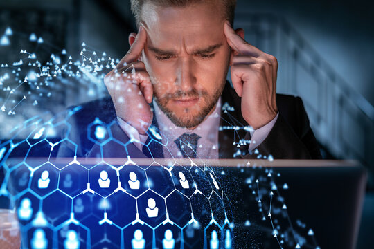 Handsome businessman in suit at workplace working with laptop to hire new employees for international business consulting. HR, social media hologram icons over office background