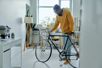 Cheerful young multiracial man examining his bicycle while standing in office