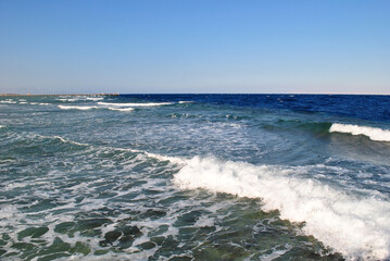 Foamy waves roll on the shore. In the distance the sea is bluer