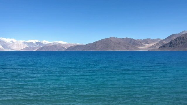 Aerial view by drone of beautiful Pangong Lake, the world’s highest saltwater lake which seems to be dyed in blue, surrounded by amazing snow mountains range with a clear blue sky in the background