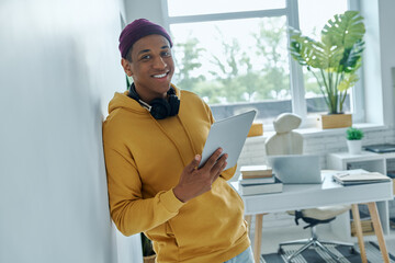 Happy mixed race man holding digital tablet while standing near his working place