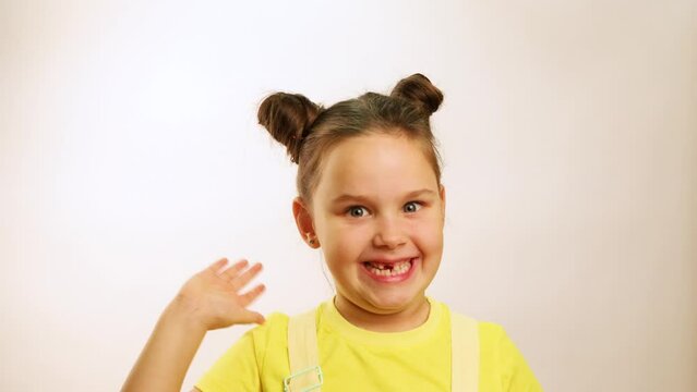 Little funny girl wide smiling with gap in mouth from fallen tooth and emotionally waving hand closeup, white background. Joyful toothless child. Concept of healthy teeth and beautiful smile.