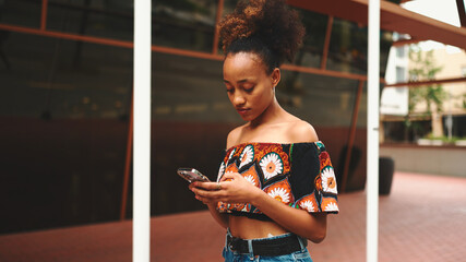 Close-up African girl with ponytail wearing in crop top with national pattern walks smiling down...