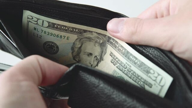 A man opens a black wallet with a 20 dollar bill inside on a white background. 