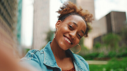 Closeup portret cute African girl with ponytail, wearing denim jacket makes stream, video call on smartphone in modern city background. - obrazy, fototapety, plakaty