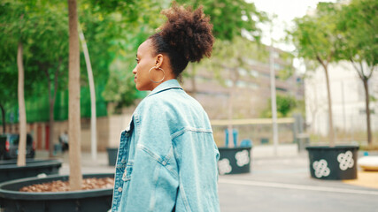 Cute African girl with ponytail, wearing denim jacket, in crop top with national pattern, walking down the street.