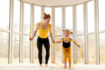 Young fit mom and her daughter having fun with hula hoop in a gym