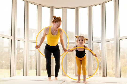 Young Fit Mom And Her Daughter Having Fun With Hula Hoop In A Gym