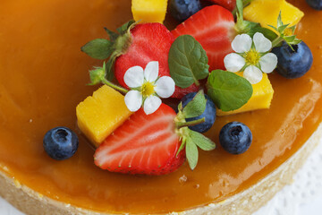 Mango cheesecake decorated with berries, mango slices and flowers on a stand. Close-up
