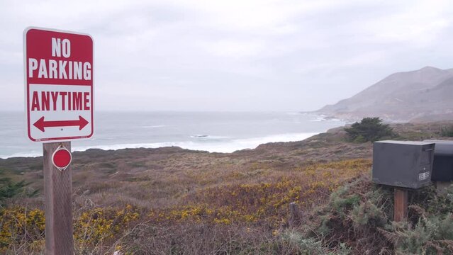 No parking any time road sign on pacific coast highway 1. Postbox or mailbox, Cabrillo road. Ocean sea waves on Garrapata beach, California, Big Sur nature trail, USA. Mountains, foggy misty weather.