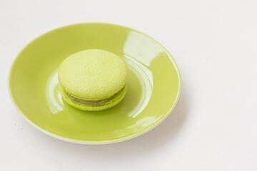 Green macaron on a green plate on white background. Pistachio nut macaroon