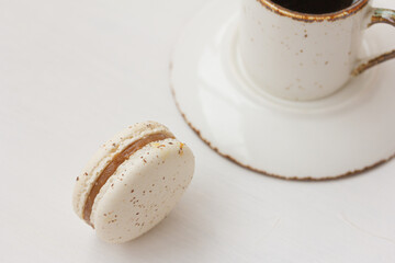 White macaron, cup of coffee on white background. Salted caramel macaroon