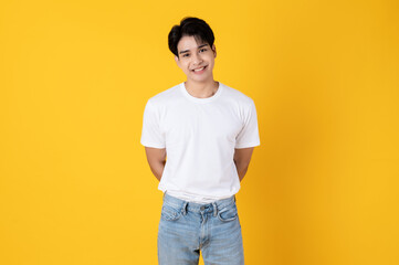 Fototapeta na wymiar Smiling young asian teenage man wearing white shirt and jeans on yellow background