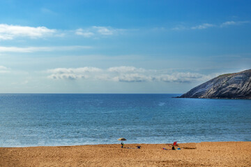 Fototapeta na wymiar Pusta plaża, samotny parasol, morze, w tle wyskoki klif oraz niebo. Wakacje.
