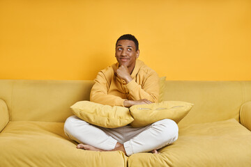 Thoughtful mixed race man relaxing on the couch with yellow background