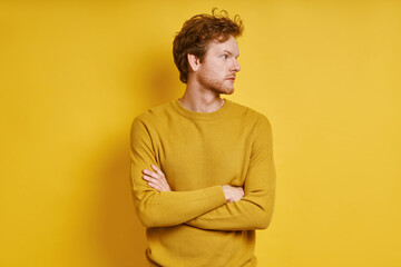 Confident redhead man keeping arms crossed while standing against yellow background