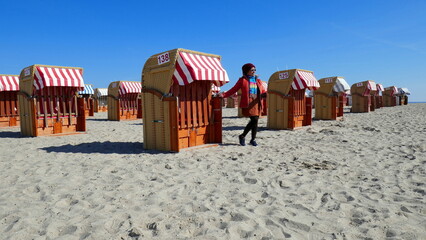 Fr&ouml;hliche h&uuml;bsche Asiatin betrachtet den Sandstrand an der Ostsee bei Travem&uuml;nde mit vielen Strandk&ouml;rben 