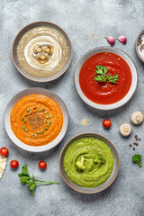 A set of colored vegetable soups in bowls. Various vegan soups with ingredients. Gray concrete grunge background. Top view, vertical photo.