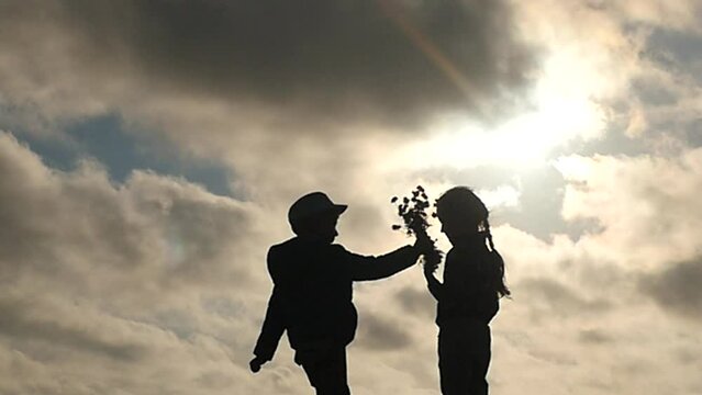 small boy presenting flowers and kissing young girl silhouettes slow-motion - love concept