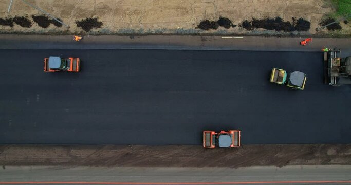 Road construction works aerial view. Laying of new asphalt on the road. The paver lays fresh asphalt, road rollers level and compact asphalt. Road construction equipment, view from a height