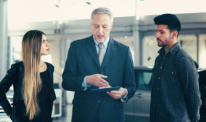 Car dealer exaplining a car's features to a couple by reading a document