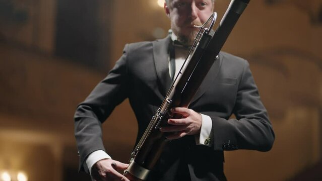 man with bassoon is playing music in scene of classical music hall, musician in black suit