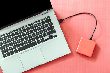 Close-up, top view of a power bank connected to a laptop, on a red background.