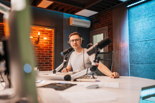 The DJ hosts the program and communicates with the audience on air at the radio station. The announcer reads the news. A male radio host speaks into a microphone and records a podcast