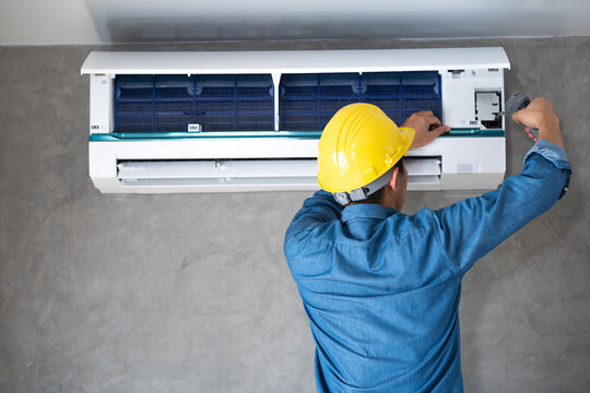 Technician man repairing ,cleaning and maintenance Air conditioner on the wall with screw driver in bedroom or office room.On site home service,Business ,Industrial concept.