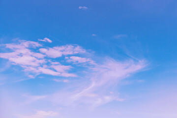 Blue sky with beautiful light pink and red cirrus clouds on a warm sunny day as an abstract background.