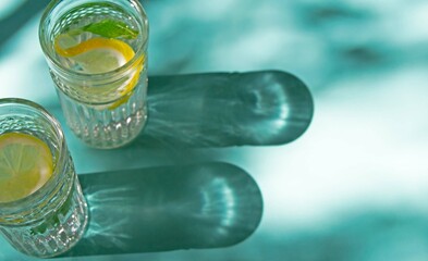 Two glasses with a refreshing drink with lemon and mint on a sea-green background with sparkling shadows from the glass.
