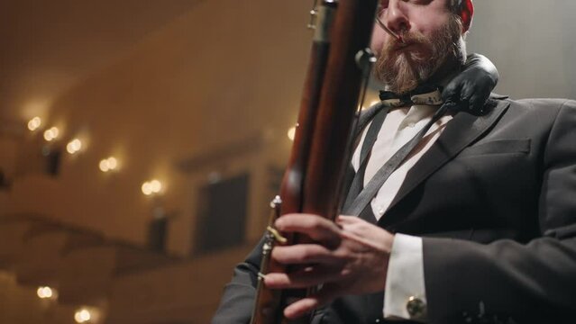 adult man with bassoon is playing music on scene of old music hall, classic music concert in opera house