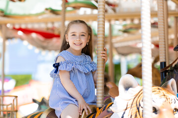 Adorable little girl in blue dress at amusement park having a ride on the merry-go-round