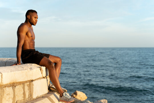 Multiracial man looking away while sitting near the sea and enjoying of the views