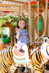 Adorable little girl in blue dress at amusement park having a ride on the merry-go-round