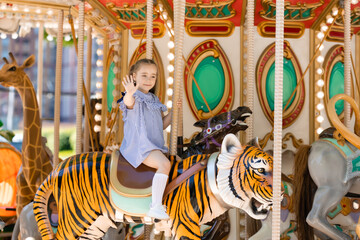 Fototapeta na wymiar Adorable little girl in blue dress at amusement park having a ride on the merry-go-round