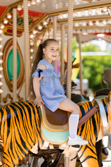 Adorable little girl in blue dress at amusement park having a ride on the merry-go-round