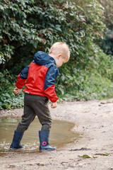 Playful boy splashing water in puddle on road.