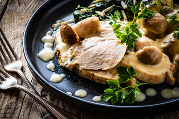 Roast pork ham in mushroom sauce with boiled potatoes and cooked spinach on wooden table
