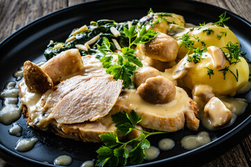 Roast pork ham in mushroom sauce with boiled potatoes and cooked spinach on wooden table
