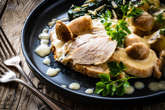 Roast pork ham in mushroom sauce with boiled potatoes and cooked spinach on wooden table
