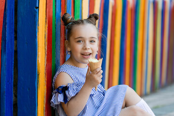 Cute little girl in blue dress eating ice cream in park summertime colorful background