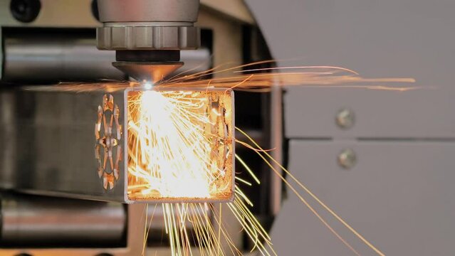 Close up: automatic cnc laser cutting machine working with metal square pipe with many sparks at factory, plant. Metalworking, industrial, manufacturing, technology and equipment concept