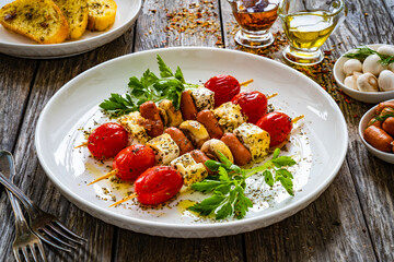 Sausage skewers - fried sausages with feta cheese, mushrooms and cherry tomatoes on wooden table

