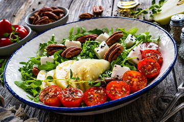 Fresh salad - goat cheese, pear and vegetables on wooden table
