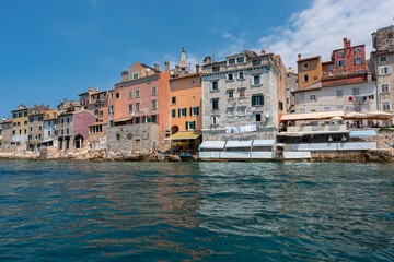 Old Croatian Rovinj city view from the sea with laundry drying by the windows and people on the cafe terrasses enjoying the view. 2022