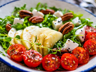 Fresh salad - goat cheese, pear and vegetables on wooden table
