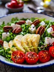 Fresh salad - goat cheese, pear and vegetables on wooden table
