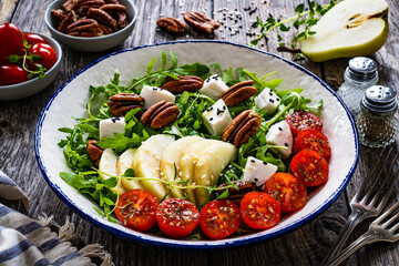 Fresh salad - goat cheese, pear and vegetables on wooden table
